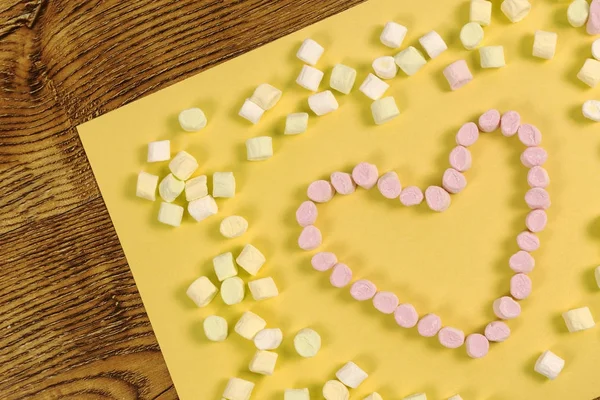 Marshmallow-Bonbons in Herzform platziert. Valentinstag und Liebeskonzept auf gelbem Papier und Holzdeck Hintergrund — Stockfoto