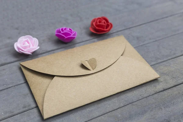 Valentine day letter. Envelope from craft paper with heart on it and three little roses flowers on wood background. Love conception.