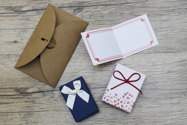Kartu kertas kosong dengan amplop coklat dan kotak hadiah buatan tangan di atas kayu . — Stok Foto