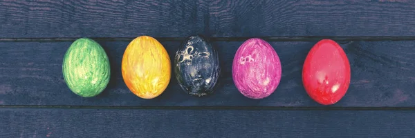Easter holiday. Colorful easter egg on dark wood. Toned.