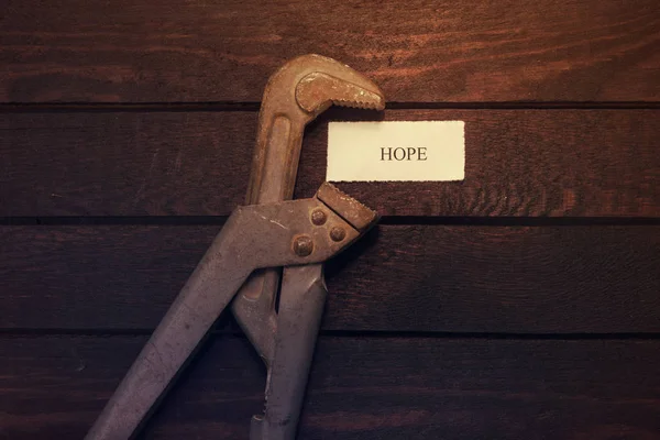Γαλλικό κλειδί σωλήνων συμπιέζει ένα κομμάτι χαρτί με μια επιγραφή ελπίδα. πιο ήπια εικόνα. — Φωτογραφία Αρχείου