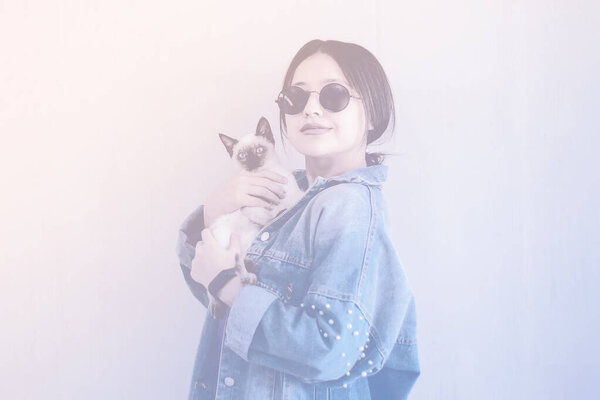 Young attractive woman hugging pussy cat in hands. Cute and glamorous girl in trendy sunglasses posing with her Siamese cat