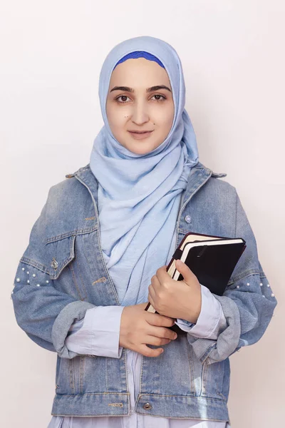 Portrait of cute Muslim businesswoman. Attractive Muslim student holding notepads. Lovely Muslim girl in hijab and denim jacket. Modern, cultural, religious and business concept — 스톡 사진