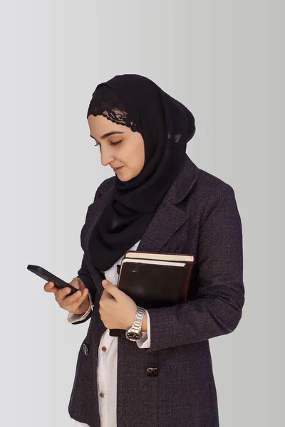 Ganska muslimsk affärskvinna i hijab innehav stack av affärshandlingar, anteckningsblock och använda smartphone, ringer till partners — Stockfoto