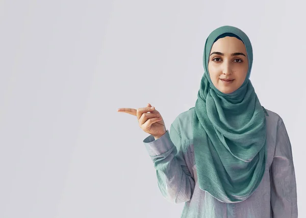 Мила мусульманка з радісним виразом обличчя відводить вказівний палець, показуючи, щоб копіювати простір на розі. Портрет мусульманської жінки з Хіджабу. — стокове фото