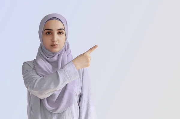 Mulher muçulmana bonito com expressão facial alegre aponta para longe com o dedo indicador, mostrando para copiar espaço na esquina. Retrato da mulher de oração muçulmana no hijab — Fotografia de Stock