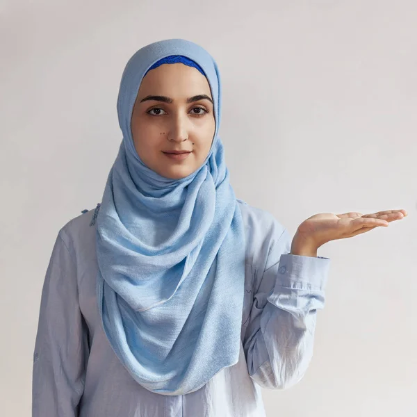 Portrait of cute Muslim woman in hijab. Copy space for text. Beautiful Muslim girl raising palm over copy space, as if holding something — 스톡 사진