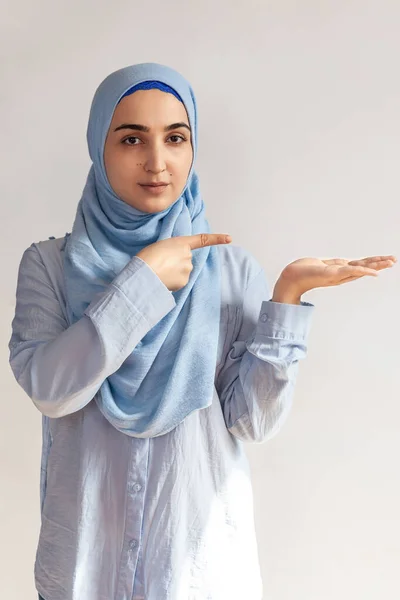 Portrait of cute Muslim woman in hijab. Copy space for text. Beautiful Muslim girl raising palm over copy space, as if holding something — Stock Photo, Image