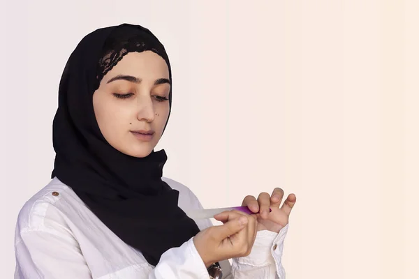 Перська жінка в Хіджабі робить манікюр з нігтями на білому. Середньосхідна самиця в Абаї виконує манікюр на собі за допомогою нігтьового файлу. — стокове фото