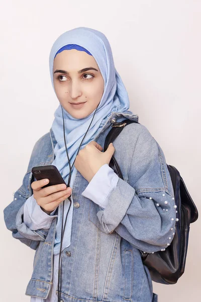 A estudante muçulmana moderna ouve música, podcasts e audiolivros no smartphone. Mulher muçulmana feliz no hijab ouvindo músicas com o fone de ouvido — Fotografia de Stock