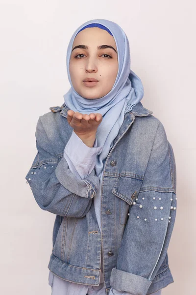Portrait of stylish Muslim girl in jean jacket sending air kiss. Modern and young middle-eastern girl in hijab sending blowing air kiss. Lovely Persian woman expressing love — Stock Photo, Image