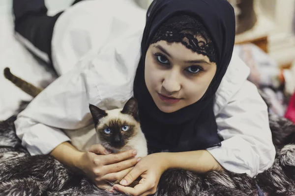 Приваблива дівчина муслім грає зі своїм екзотичним домашнім сіамським котом. — стокове фото