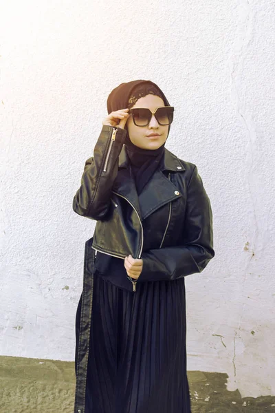 Retrato de una hermosa chica de Oriente Medio vestida con ropa islámica tradicional - hiyab. Mujer iraní moderna y joven en gafas de sol y una chaqueta de cuero —  Fotos de Stock