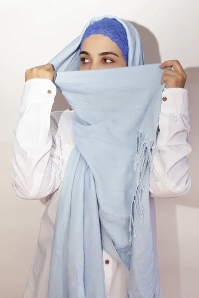 Elegant Muslim woman in white shirt and bright blue hijab. Stylish Iranian girl in Muslim clothing. Isolated portrait of attractive middle-eastern woman