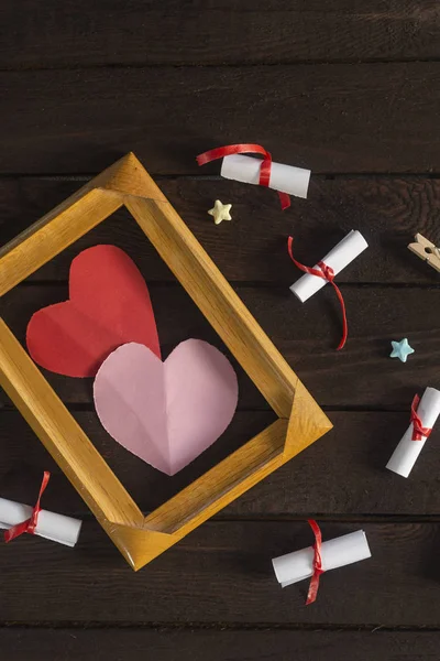 Flat lay sfondo romantico. Scatola regalo, carte augurali arrotolate e struttura in legno con cuori di carta su tavola di legno scuro . — Foto Stock