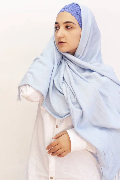 Elegant Muslim woman in white shirt and bright blue hijab. Stylish Iranian girl in Muslim clothing. Isolated portrait of attractive middle-eastern woman