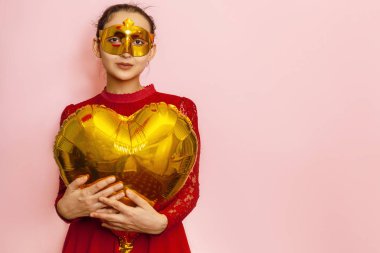 Maskeli balon giyen ve kalp şeklinde balon tutan bir kadın. Sevgililer günü, doğum günü, yıldönümü, şenlik, balo kutlaması kavramları.