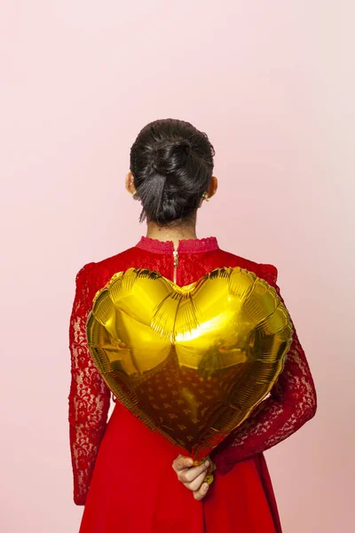 An attractive Iranian woman holds a golden heart-shaped air balloon. Celebrating Valentines day. Beautiful Happy Young middle-eastern girl. Holiday party, Anniversary, Birthday celebration