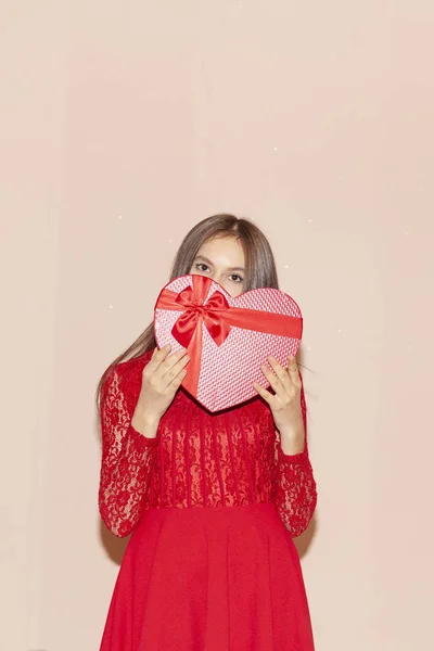 Feliz niña sostiene corazón en forma de caja de regalo. Día de San Valentín, cumpleaños, día de la mujer, aniversario, concepto de celebración de vacaciones — Foto de Stock