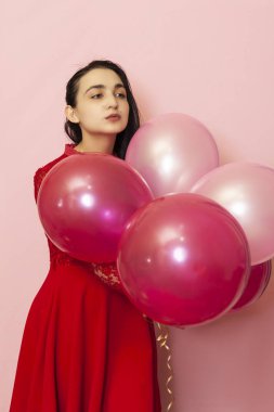 Kırmızı gece elbisesi içinde elinde balonlarla genç ve güzel bir kadın. Yirmili yaşların mutlu orta doğulu kadın portresi Sevgililer Günü, doğum günü, parti