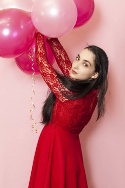 Kırmızı gece elbisesi içinde elinde balonlarla genç ve güzel bir kadın. Yirmili yaşların mutlu orta doğulu kadın portresi Sevgililer Günü, doğum günü, parti