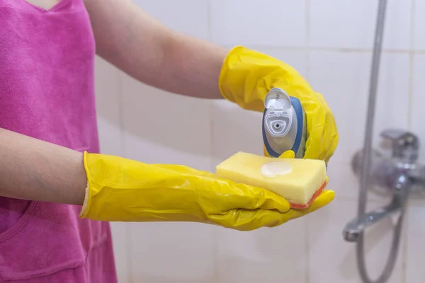 Housewife cleaning bathroom tap and shower Tap. Maid in yellow protective gloves washing dirty bath tap. Hands of woman washing or cleaning up bath