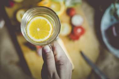 Bir bardak taze su ve bir dilim limon tutan tanınmamış bir kadın eli. Diyet, organik ve sağlıklı gıda konsepti. Yukarıdan görüntüle.