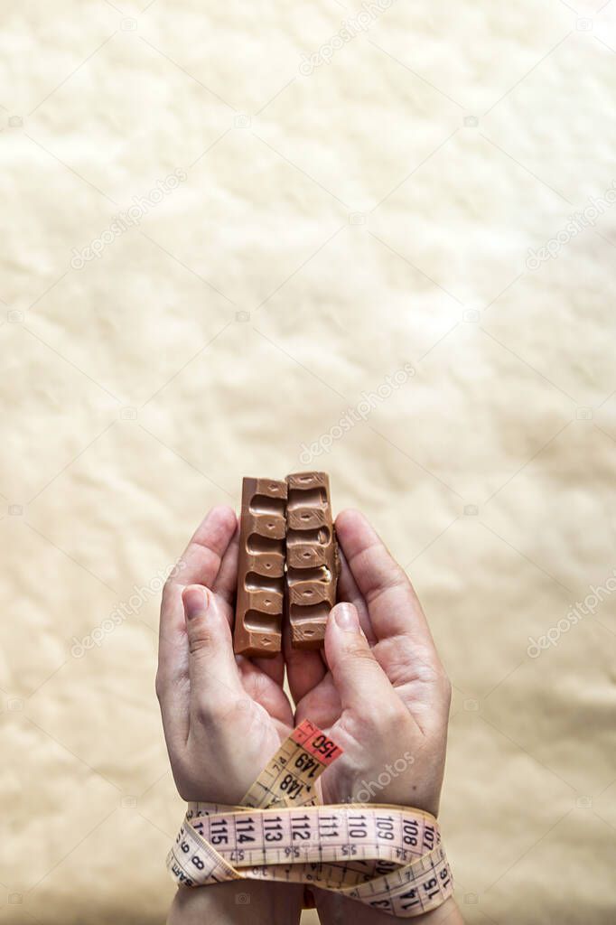 Hands of plus size woman tied with measuring tape and holding chocolate. Weight loss problems. Plus size woman cant stop unhealthy eating