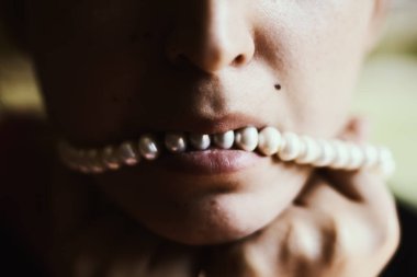 İncilerle bağlanmış kadın ağzı. Seks kölesi. Dudaklarında beyaz kolye olan kadın dudaklarının yakın plan fotoğrafı.