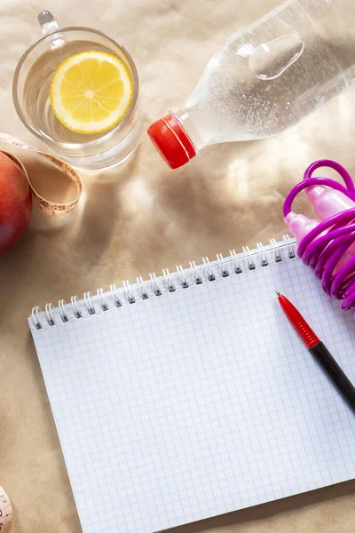 Diet planning. Meal plan - healthy food: Fresh water bottle, skipping rope and an apple with an empty notepad