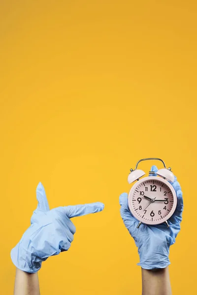 目覚まし時計を持っている保護医療用手袋の手 コロナウイルスのパンデミック ウイルス感染が広がるか またはコロナウイルスワクチンを開発するために急いでいる間 家に帰る時間 死亡者数の増加 — ストック写真
