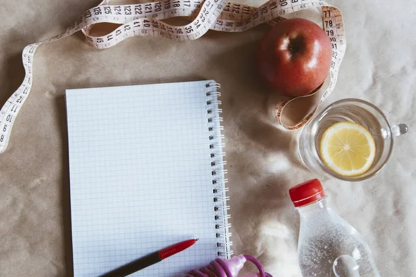 Diet planning. Meal plan - healthy food: Fresh water bottle, skipping rope and an apple with an empty notepad