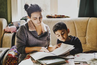 Ebeveynlik ev ödevlerinde yardımcı oluyor. Küçük oğlunun ödevlerini yapmasına yardım eden genç bir annenin otantik fotoğrafı.