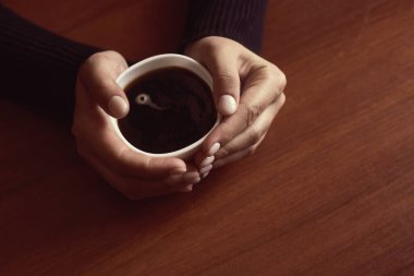 Kahve dükkanındaki kadın. Sıcak ev ortamında kahve içen tanınmamış bir kadın. Ahşap masa arkasında kahve fincanı tutan kadın eller.