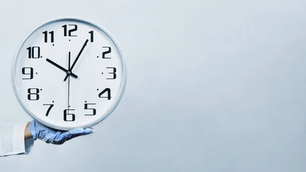 Tıbbi koruyucu maskeli ve eldivenli kadın bir doktor büyük bir saat tutuyor. Bilim adamları ve virolog Coronavirus aşısı araştırması için acele ediyorlar. Sağlık çalışanları covid-19 aşısını araştırıyor.