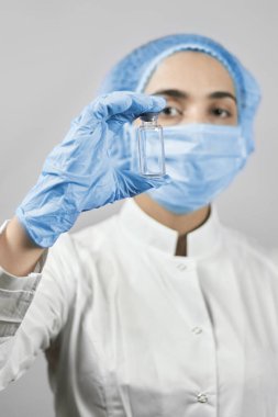 Tıbbi koruyucu maske takan kadın doktor, bilim adamı ya da virolog ve uzun araştırmalardan sonra koronavirüs aşısı tutan eldivenler. Sağlık çalışanı elinde kovid 19 aşısı tutuyor.