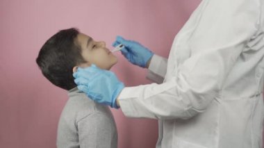 Anaokulu çocuğunun boğazını kontrol eden kadın doktor.