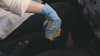 Covid-19 - Araba Dezenfeksiyonu. Arabanın vites kolunu temizliyorum. Korunaklı maske takan genç bir kadın ve eldivenler Coronavirus vites dezenfekte ediyor.