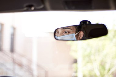 Coronavirus salgını sırasında araba süren cerrahi maske ve eldivenli genç bir kadın. Koruyucu giysili bir kadın sürücü, covid-19 virüsünü önlüyor.