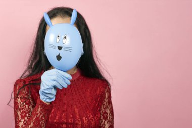 Tıbbi eldivenli ve cerrahi maske takan sevimli Paskalya tavşanı tutan bir kadın. 2020 Paskalyasını karantinada kutlayan kadın. Paskalya tatilini evde kutlayın.