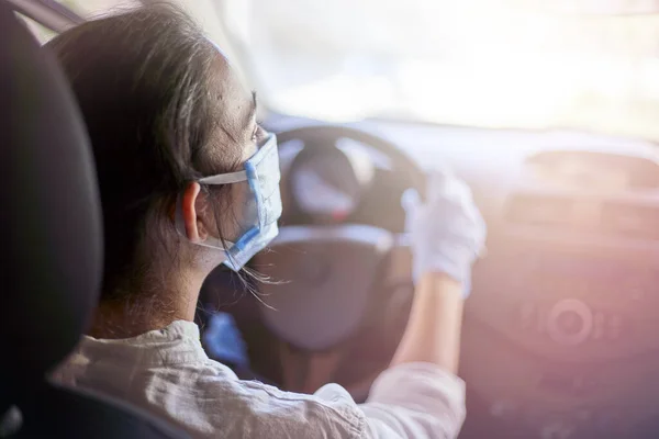 Coronavirus salgını sırasında araba süren cerrahi maske ve eldivenli genç bir kadın. Koruyucu giysili bir kadın sürücü, covid-19 virüsünü önlüyor.