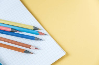 Okul malzemeleri sarı üzerine. Okul geçmişine geri dönelim. Not defteri ve renkli kalemler yığını. Uzaklık eğitimi, karantina eğitimi, ev kavramlarından öğrenme ve öğrenme