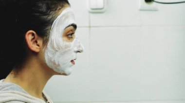Banyoda makyaj maskesi takan bir kadın. Karışık ırk dişileri yüzüne beyaz besleyici maske ya da krem sürerler. Yüzüne fırça maskesi takıyorum. Cilt temizleme spa rahatlama konsepti