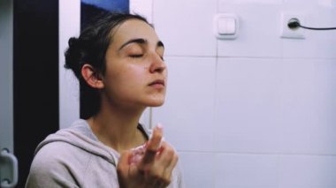 Banyoda makyaj maskesi takan bir kadın. Karışık ırk dişileri yüzüne beyaz besleyici maske ya da krem sürerler. Yüzüne maske takıyorum. Cilt temizleme spa rahatlama konsepti