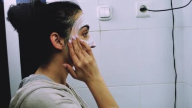 Banyoda makyaj maskesi takan bir kadın. Karışık ırk dişileri yüzüne beyaz besleyici maske ya da krem sürerler. Yüzüne maske takıyorum. Cilt temizleme spa rahatlama konsepti
