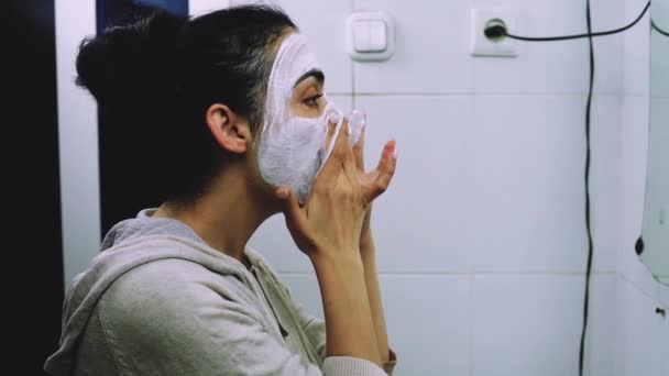 浴室で顔の化粧品マスクを適用する女性 混合人種の女性は 顔に白い栄養マスクやクリームを適用します マスクを顔に塗る スキンケアクレンジングスパ リラックスコンセプト — ストック動画