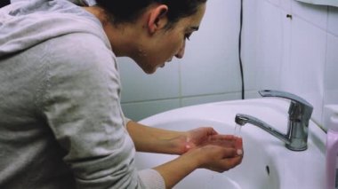 Genç melez kadın yüz maskesi yıkıyor. Yüz kozmetik maskesini temizliyorum. Cilt temizleme spa rahatlama konsepti