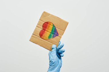 LGBTQ dostu sağlık çalışanı elinde kalp şeklinde gökkuşağı bayrağı olan el yapımı bir pankart tutuyor. LGBTQ doktoru Coronavirüs 'e karşı cephede savaşıyor.