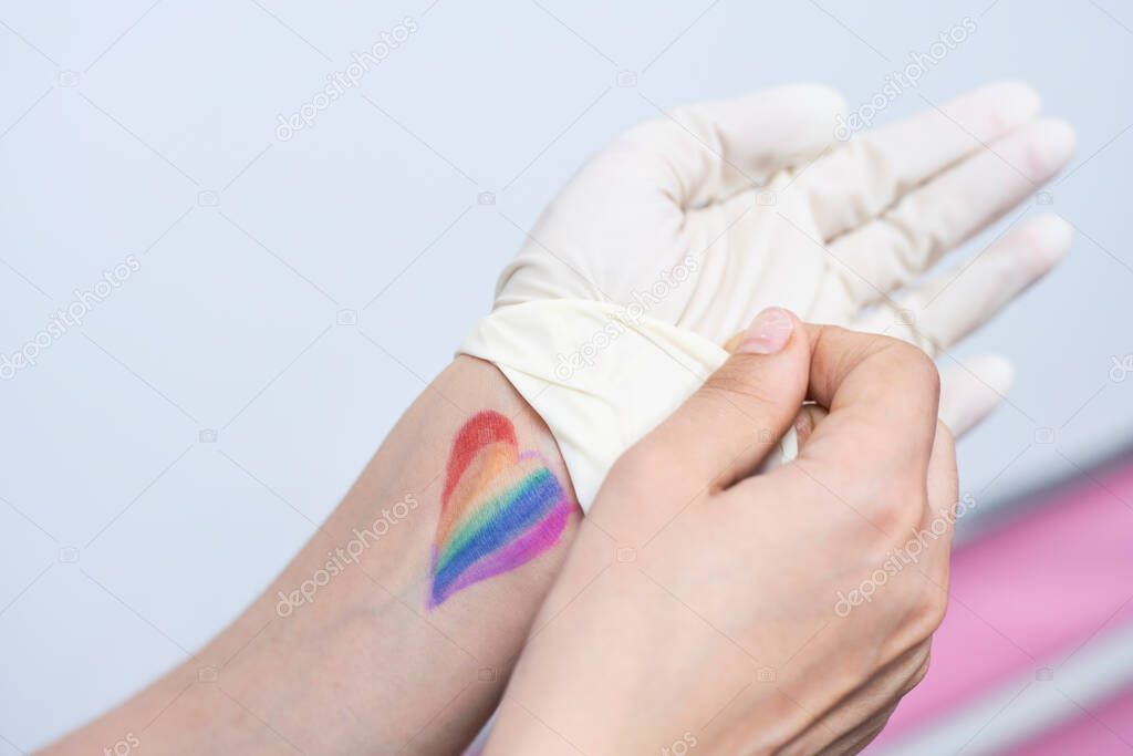 LGBTQ female doctor fights with coronavirus on frontline. LGBTQ friendly healthcare system worker with rainbow flag on wrist. LGBTQ friendly doctor or healthcare provider takes off surgical gloves