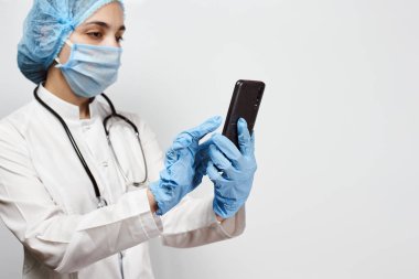 Koruyucu tıbbi teçhizat içinde, cep telefonu tutan bir sağlık çalışanı. Mola sırasında kadın doktor. Hemşire zoom video aracılığıyla ailesiyle konuşuyor.